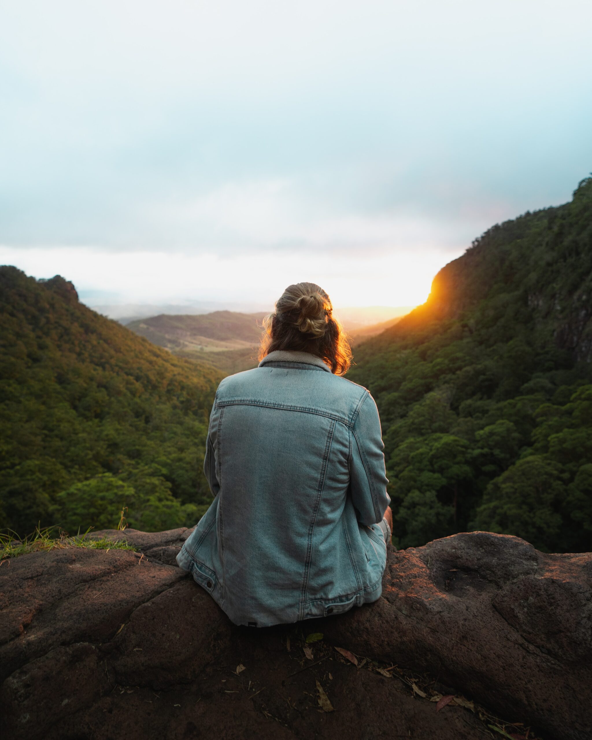 woman sitting on edge of ledge above forest